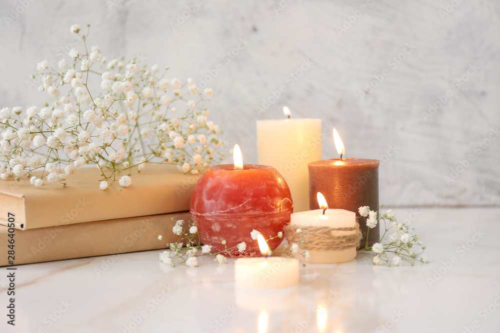 Beautiful burning candles, books and flowers on table