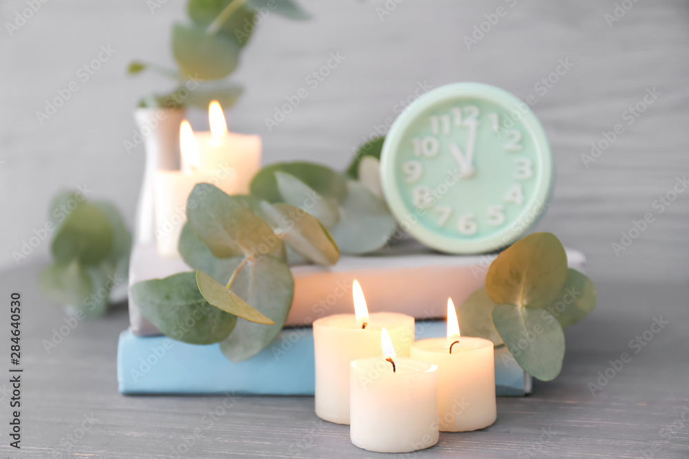 Beautiful burning candles, eucalyptus branches, clock and books on table