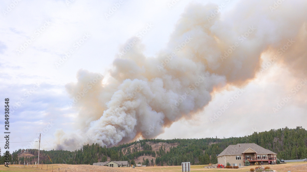 Thick black smoke rising from forest fire on the hills above the small village