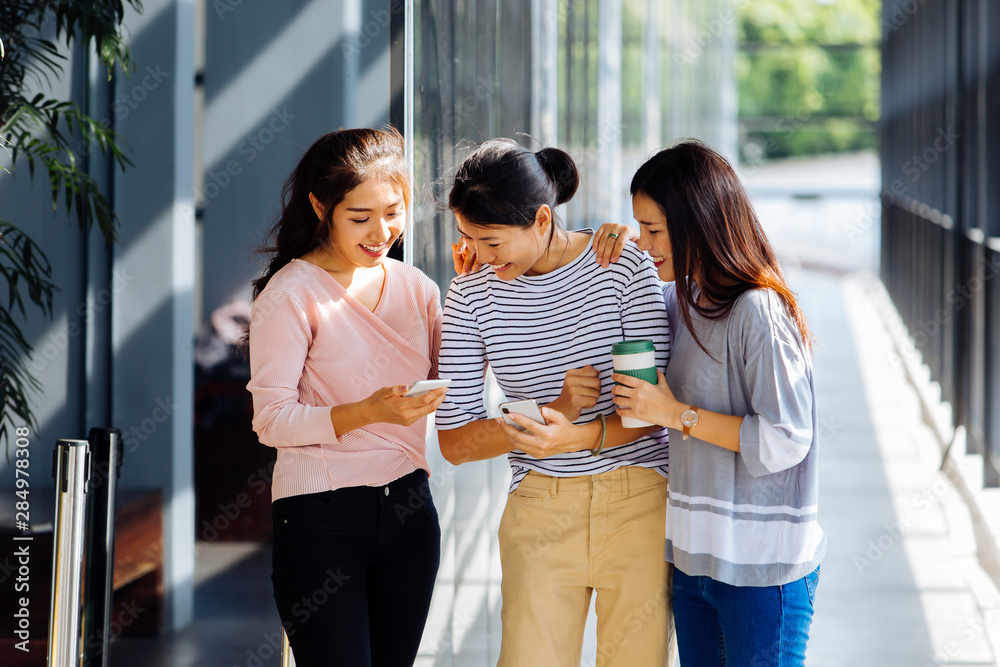 Young Asian business women talking and showing phone screen in office building in casual wear. Three