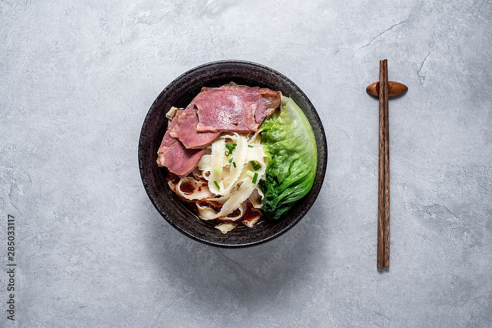 A bowl of nutritious and delicious beef noodles with noodles on a cement texture background