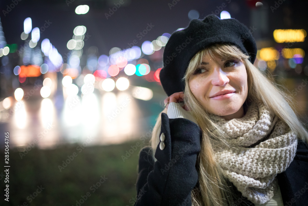 Pretty young stylish woman walking in the night city streets, bokeh illumination background