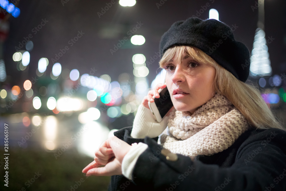 Pretty young stylish woman walking in the night city streets using modern smartpone, bokeh illuminat