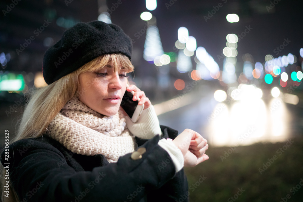 漂亮年轻时尚的女人走在夜城的街道上，使用现代的智能手机，bokeh照明