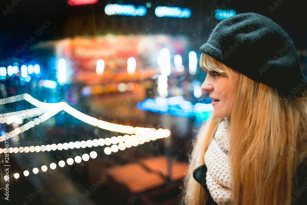 Happy smiling stylish woman walking on illuminated city street during Christmas night