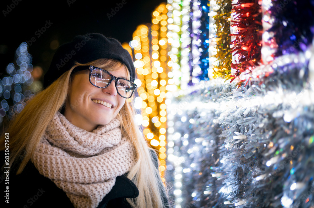 Happy smiling stylish woman walking on illuminated city street during Christmas night