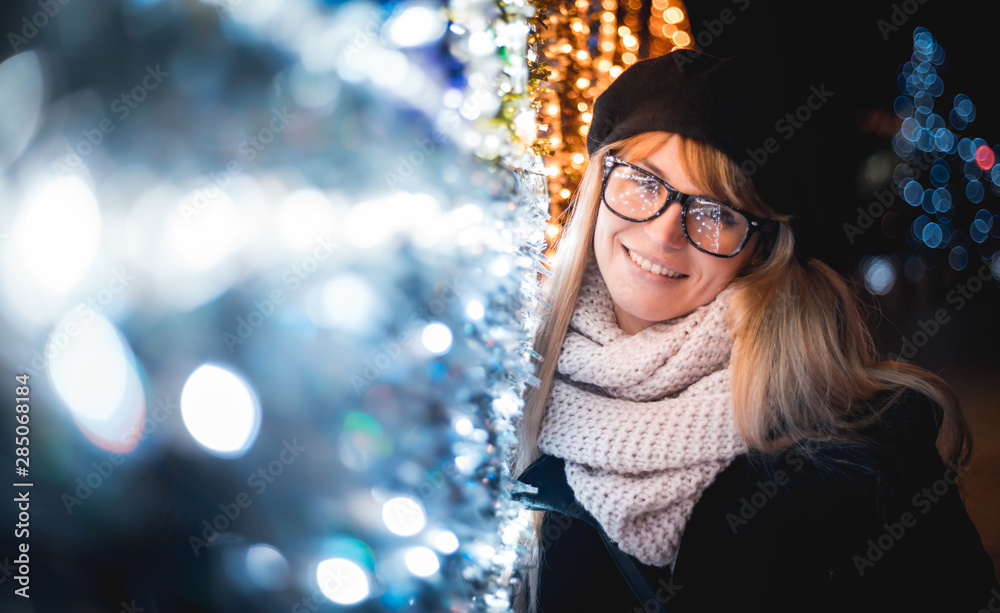 Happy smiling stylish woman walking on illuminated city street during Christmas night