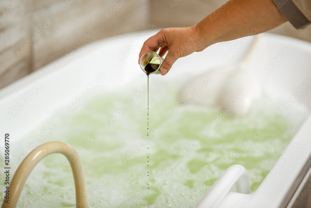 Pouring special ingredient for hydromassage into the tub filled with hot water in the spa