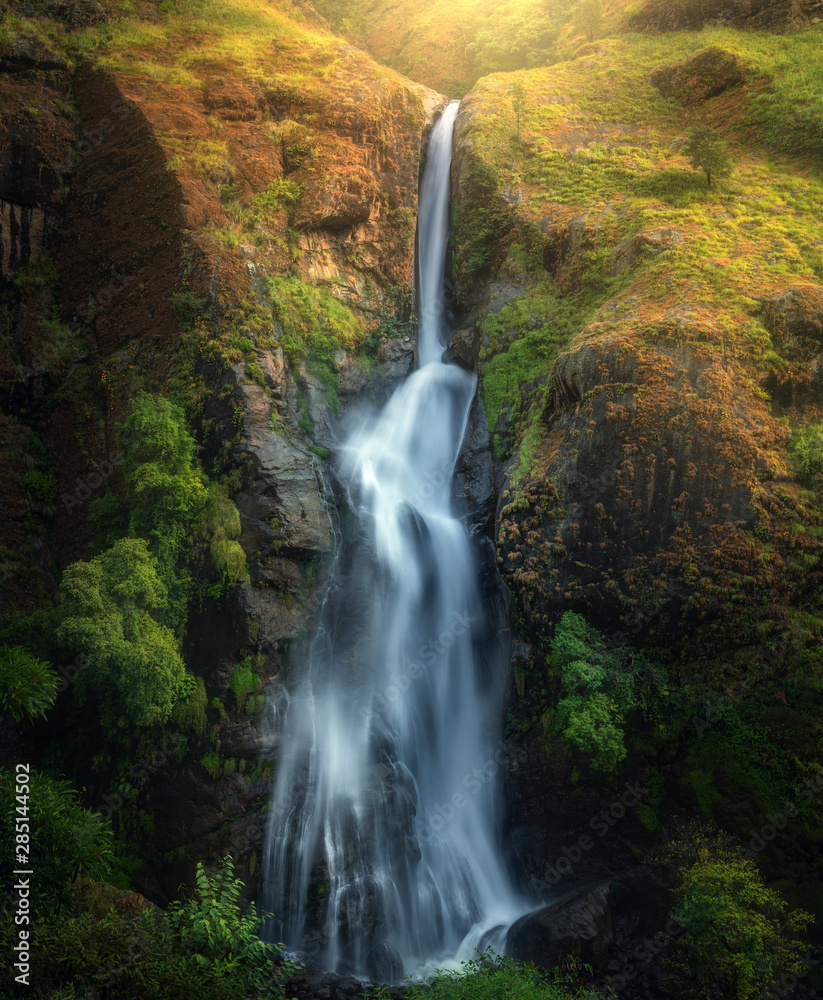 Waterfall in autumn forest at sunset in Nepal. Colorful natural landscape with waterfall with blurre