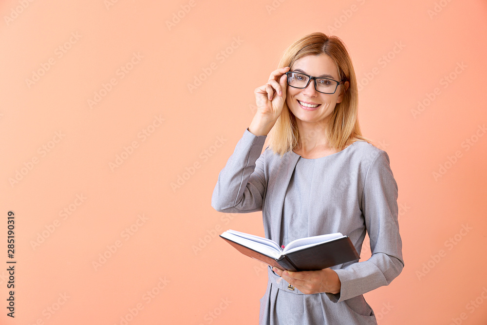 Beautiful female teacher with book on color background