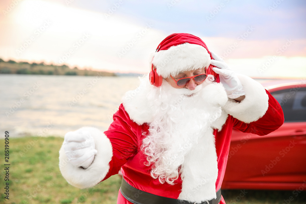 Santa Claus listening to music near car on riverside