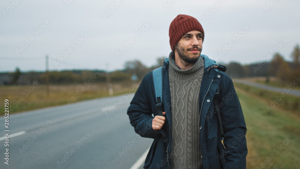 阴天，穿着休闲的搭便车旅行者坐在高速公路旁。