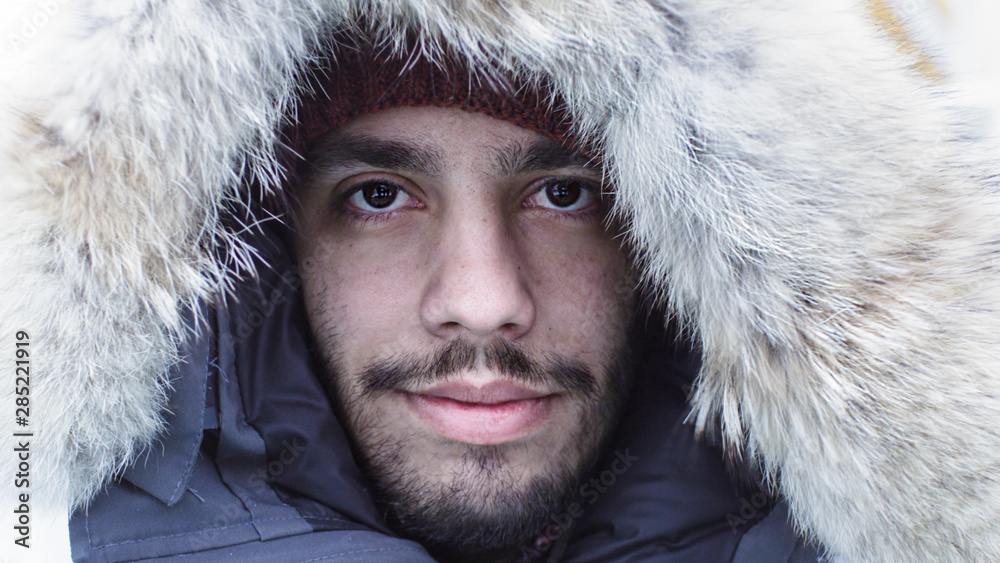 Close-up Portrait Shot of an Polar Adventurer in Warm Jacket with Fur Hood. It is Snowy and Windy