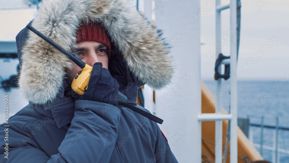 Polar Scientist in Warm Jacket Standing on Ship and Using Radio for Communication. Polar Research Ex