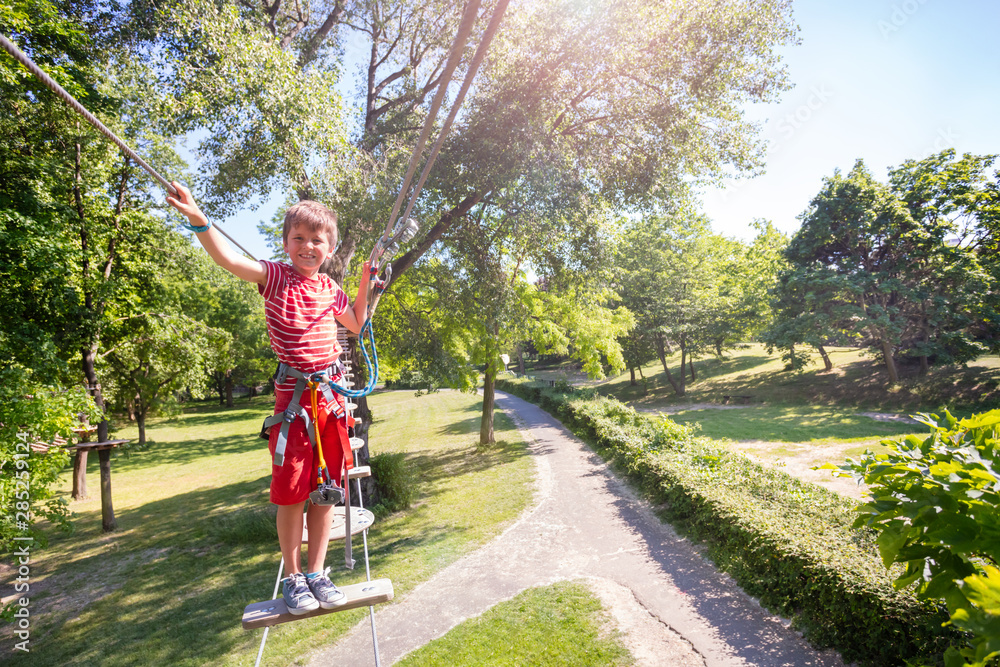 Boy walks across high rope bridge between trees