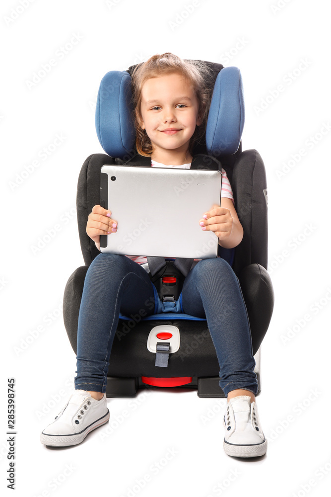 Little girl with tablet computer buckled in car safety seat against white background