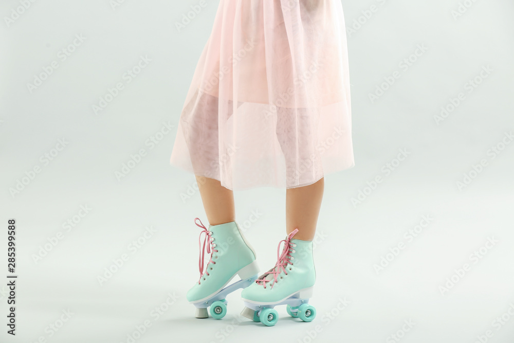 Beautiful young woman on roller skates against light background