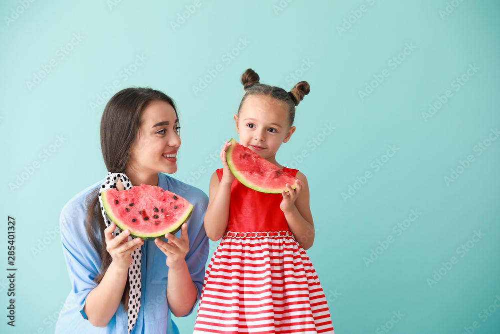 美丽的年轻女子和可爱的小女孩，彩色背景上有新鲜的西瓜