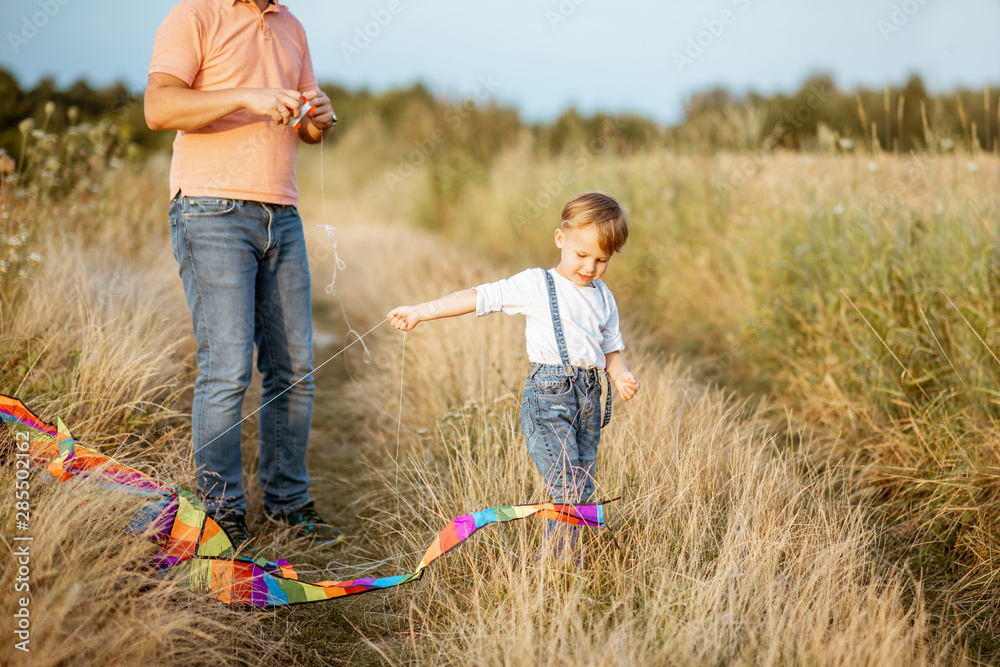 Father with son launching colorful air kite on the field. Concept of a happy family having fun durin