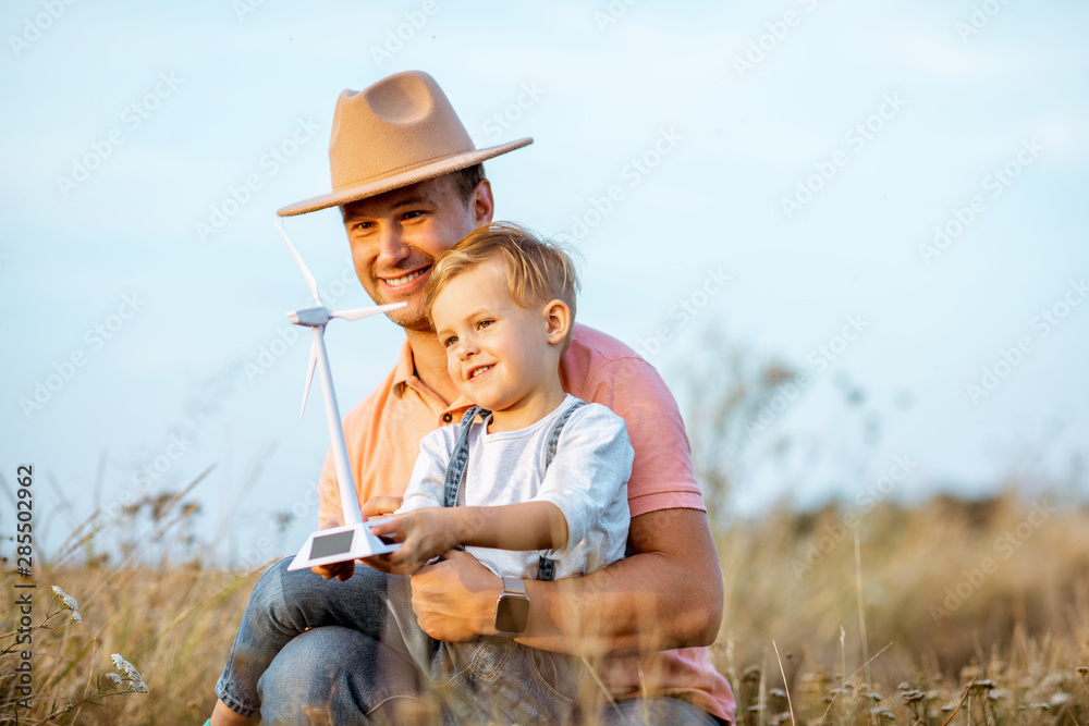 Father with young son playing with toy wind turbine in the field. Concept of knowledge of the green 