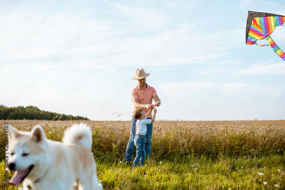 Father with son launching colorful air kite on the field during the sunset. Happy dog on the foregro