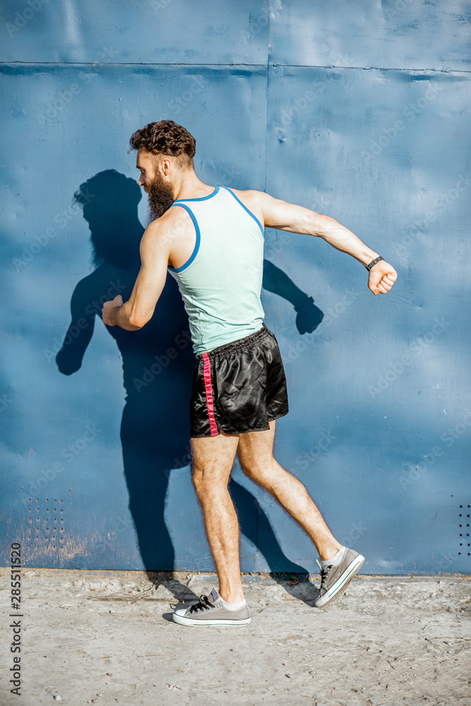 Funny portrait of an old-fashioned athlete dressed in 80s style posing on the blue wall background