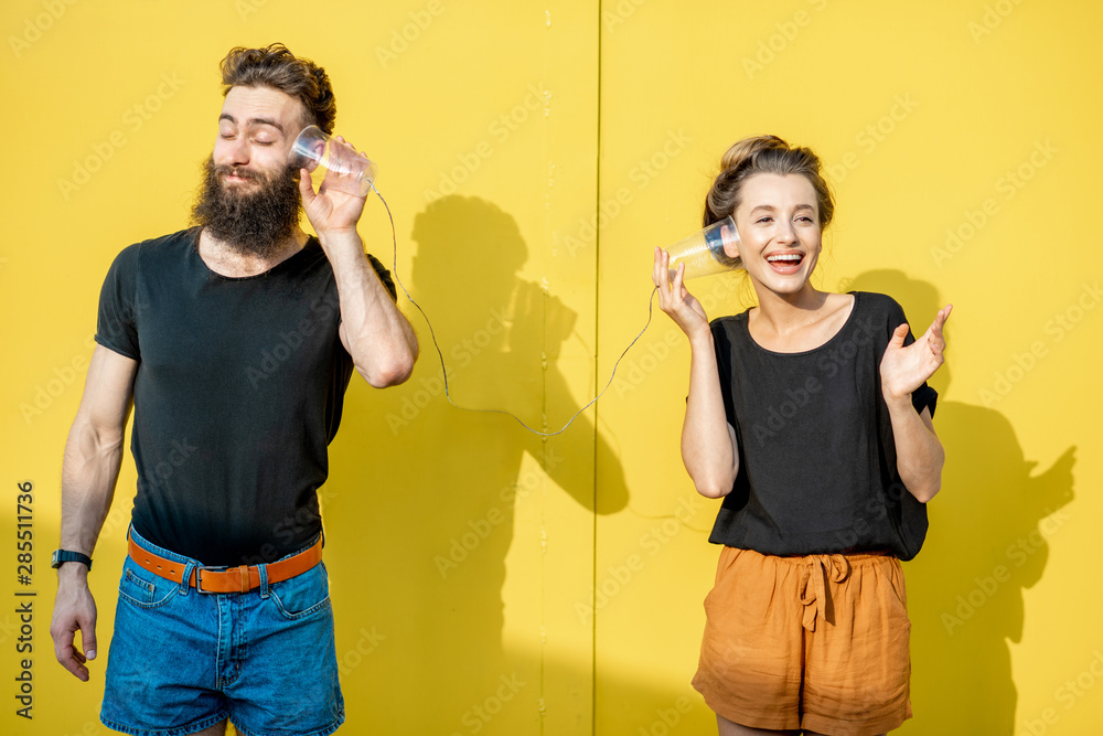 男人和女人用黄色背景上杯子做成的串电话交谈。破pho的概念