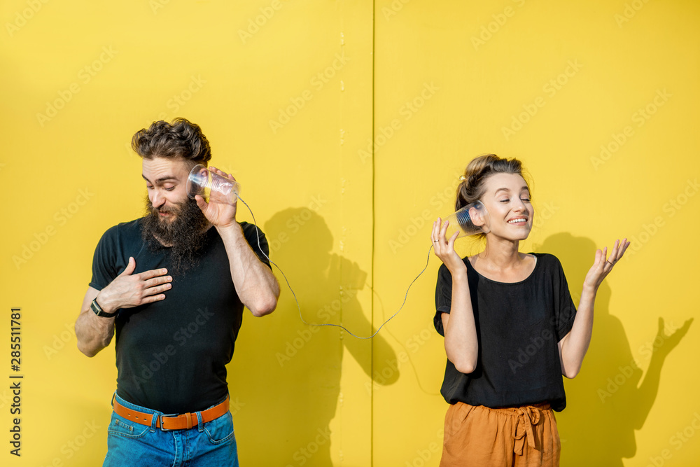 男人和女人用黄色背景上的杯子做的串电话交谈。破pho的概念