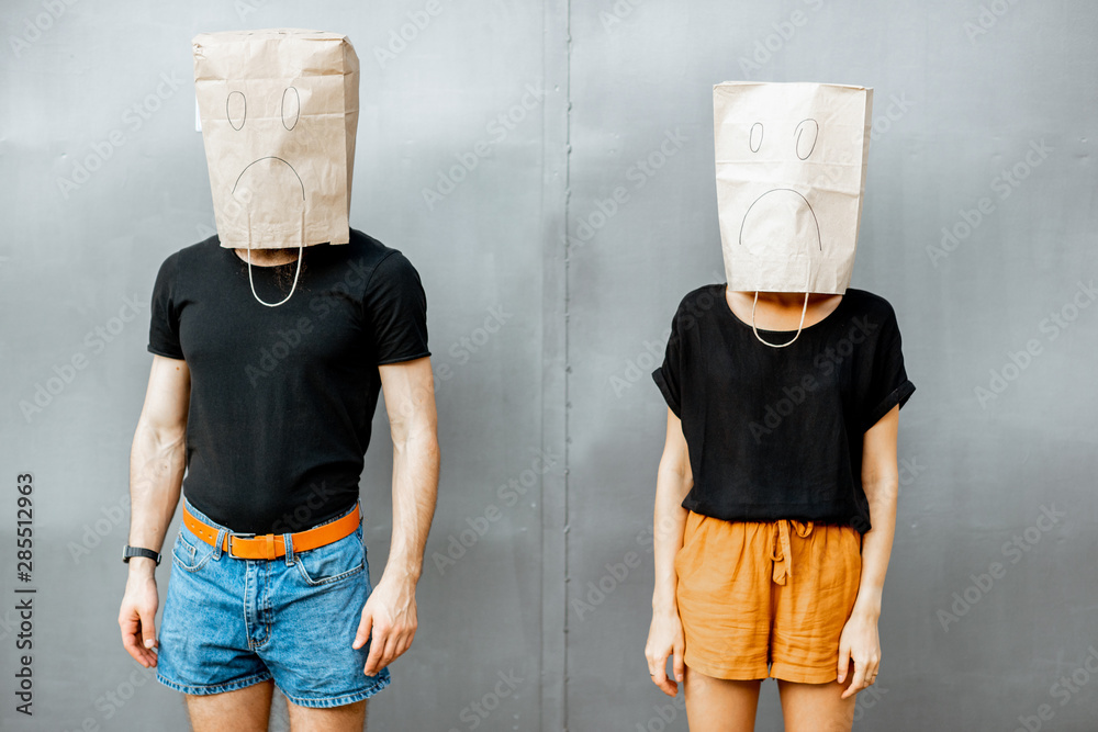 Portrait of a man and woman with paper bags on their heads on the grey wall background