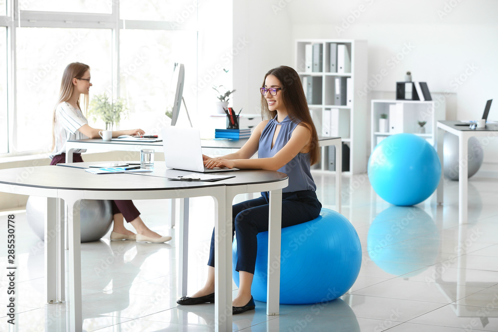 Young businesswoman sitting on fitball while working in office