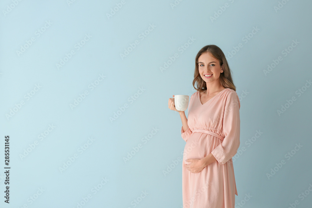 Beautiful pregnant woman with cup of tea on color background