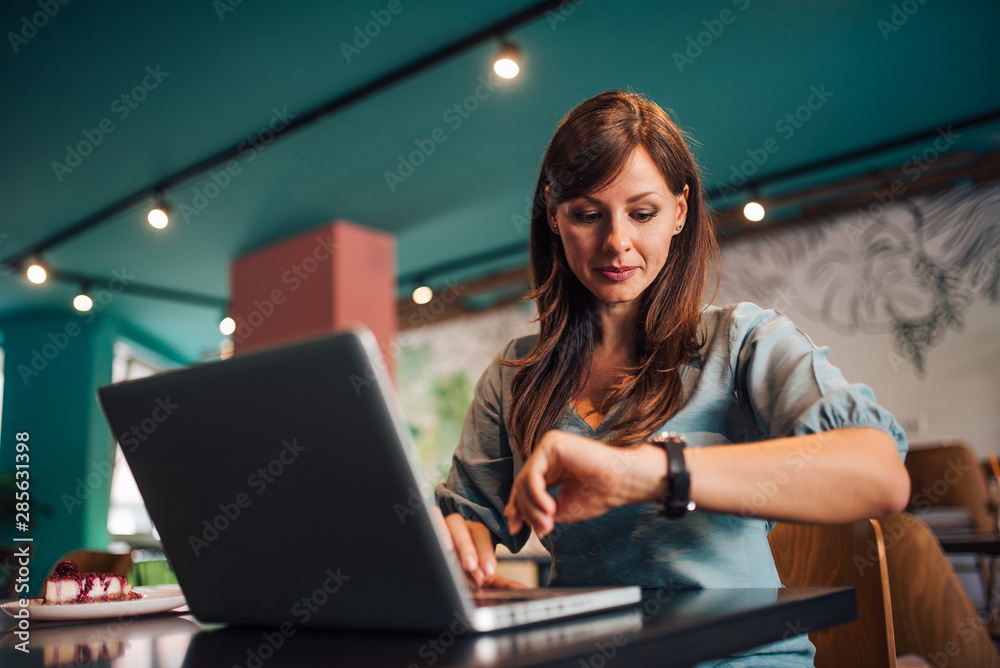 Portrait of a woman checking time on wristwatch at the cafe.