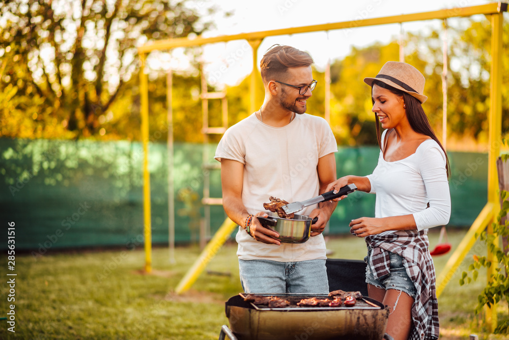 Young couple making barbecue at backyard.