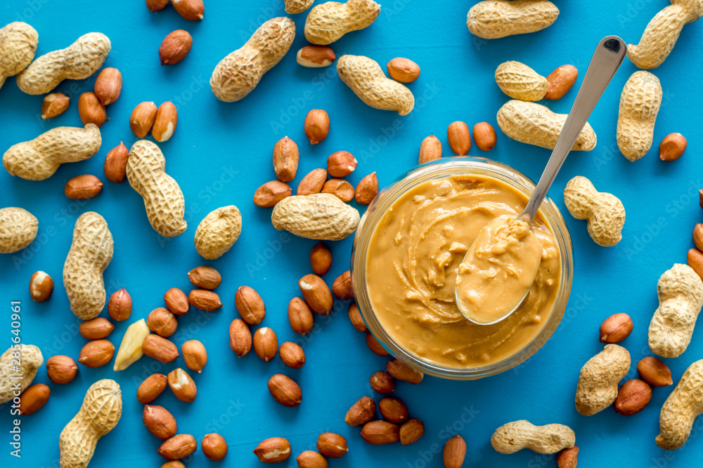 Product for hearty breakfast with peanut butter in bowl near nuts on blue background top view patter