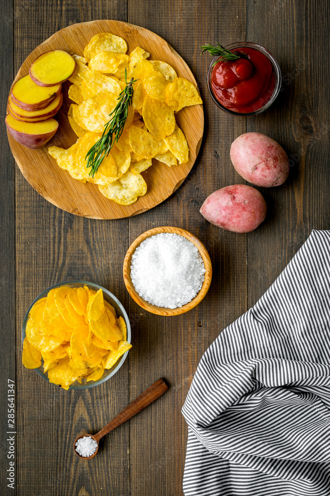 Potato crisps with fresh potato and tomato sauce on wooden background top view