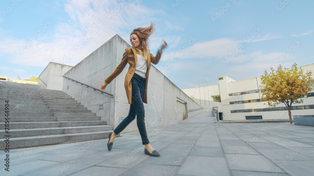 快乐快乐的年轻女子走下楼梯时积极跳舞。她穿着长款