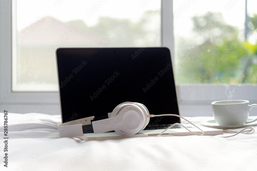 The laptop working and listen music on the white bed and coffee in the sunny day morning holiday. Mu