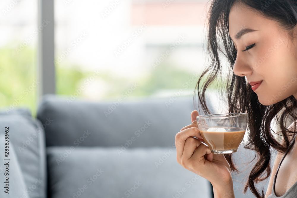 亚洲年轻女子早上坐在沙发上喝咖啡。