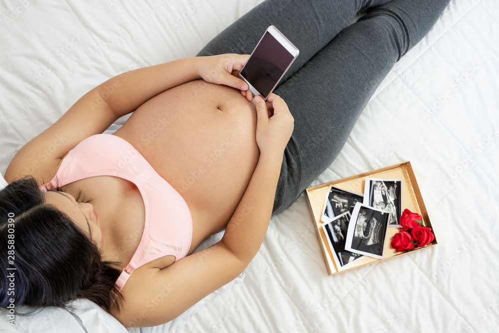 Pregnant woman feeling happy at home while taking care of her child. The young expecting mother hold