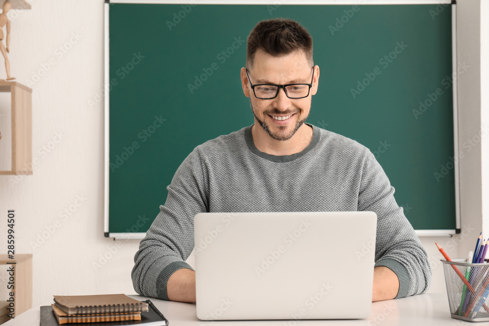 Handsome male teacher with laptop in classroom