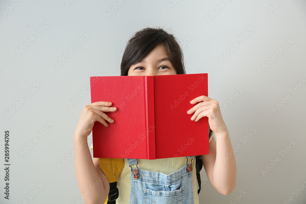 Portrait of little schoolgirl with book on light background