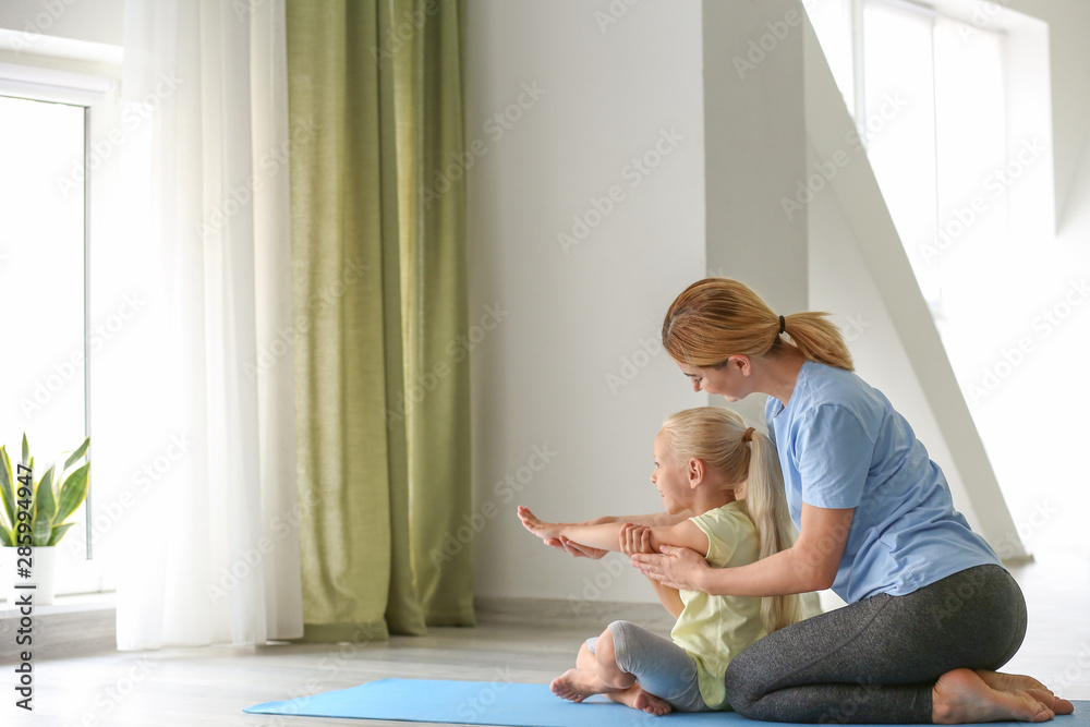 Mother helping her little girl with yoga position at home