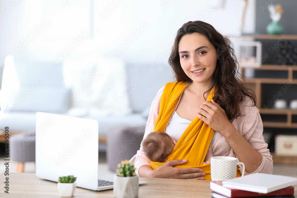 Young mother with little baby in sling working at home