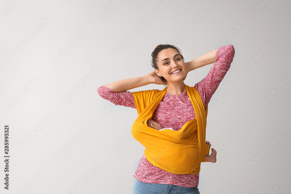 Young mother with little baby in sling on light background