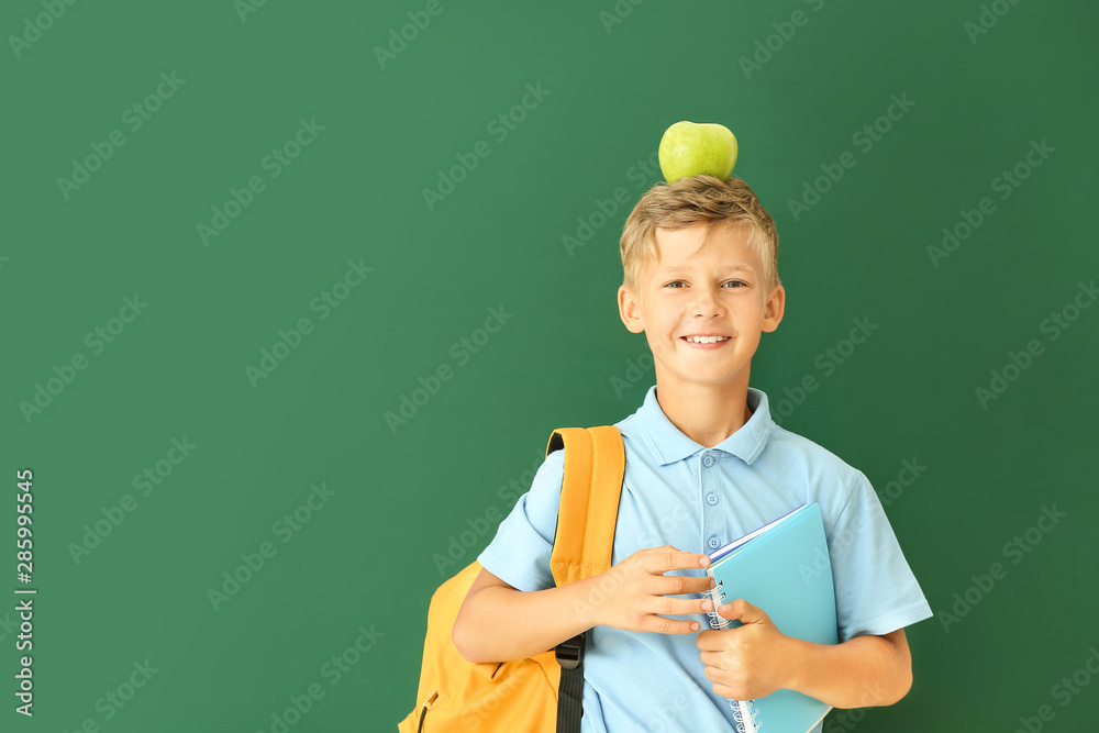 Little schoolboy with apple on color background