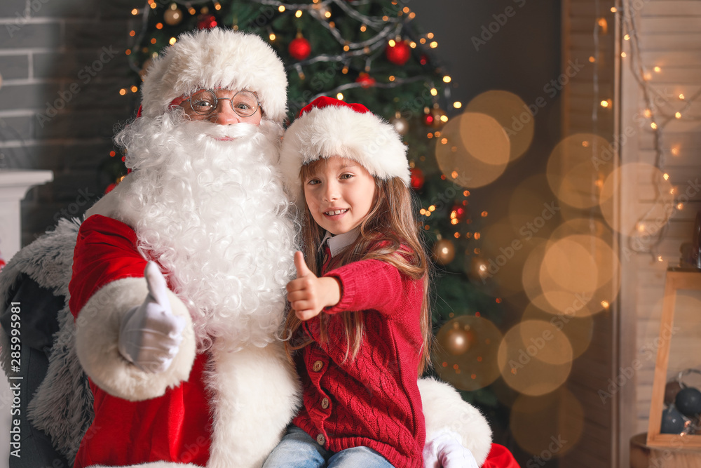 Santa Claus and little girl showing thumb-up in room decorated for Christmas