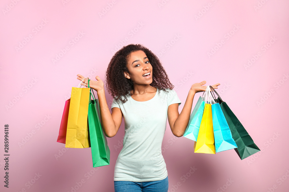 Portrait of happy African-American woman with shopping bags on color background