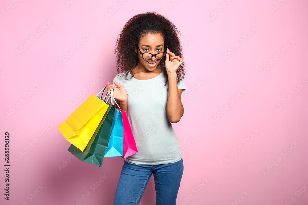 Portrait of beautiful African-American woman with shopping bags on color background