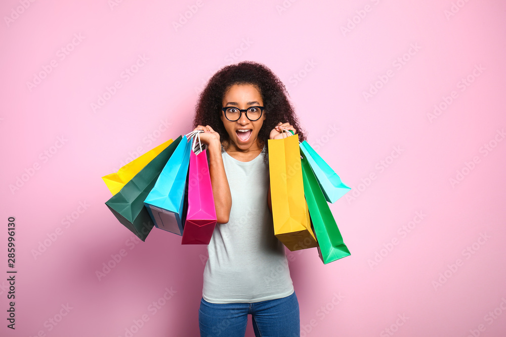 Portrait of excited African-American woman with shopping bags on color background