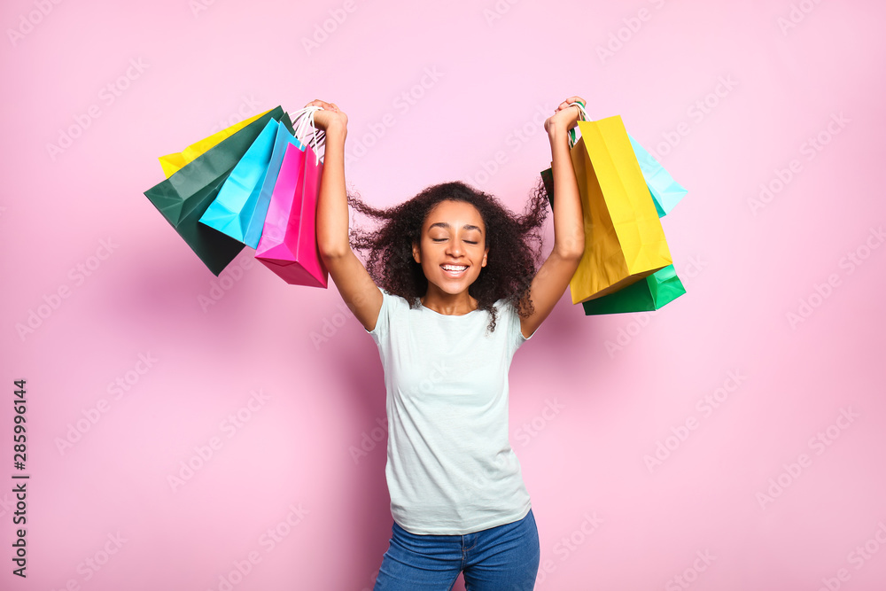 Portrait of happy African-American woman with shopping bags on color background